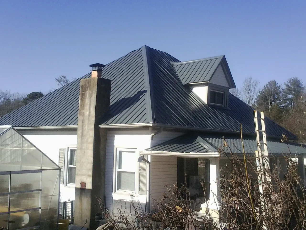 Dark blue standing seam metal roof on a white farmhouse with dormer — Slate & Tile Roof Repair by Roofing Brothers in Houlton