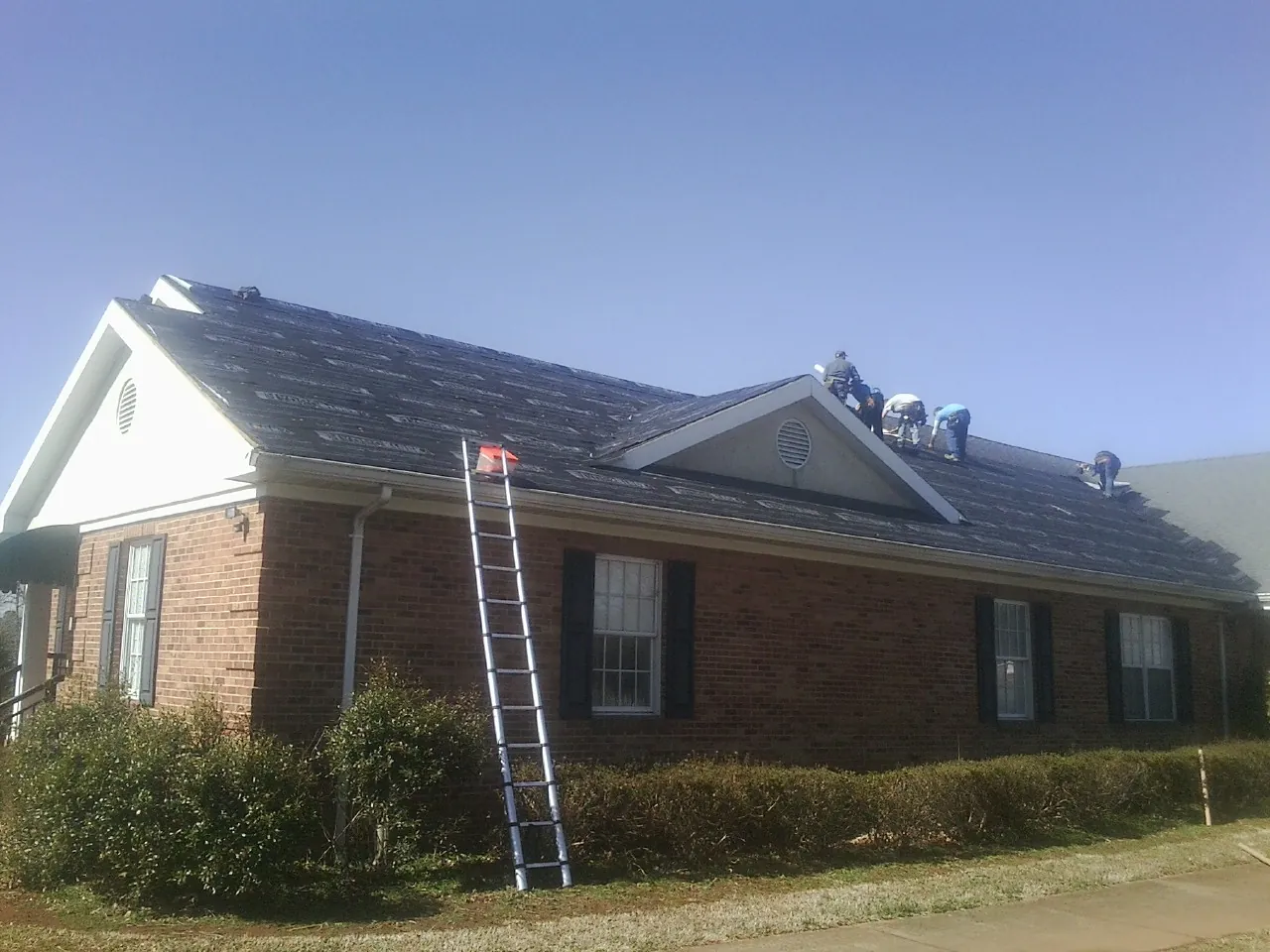 Crew tearing shingles off a brick ranch roof with a ladder set — Metal Roof Repair work by our crew in Houlton