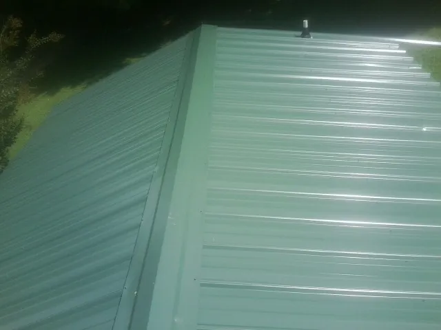 New green metal panels meeting at the ridge of a roof — Flat Roof Repair work by our crew in Houlton