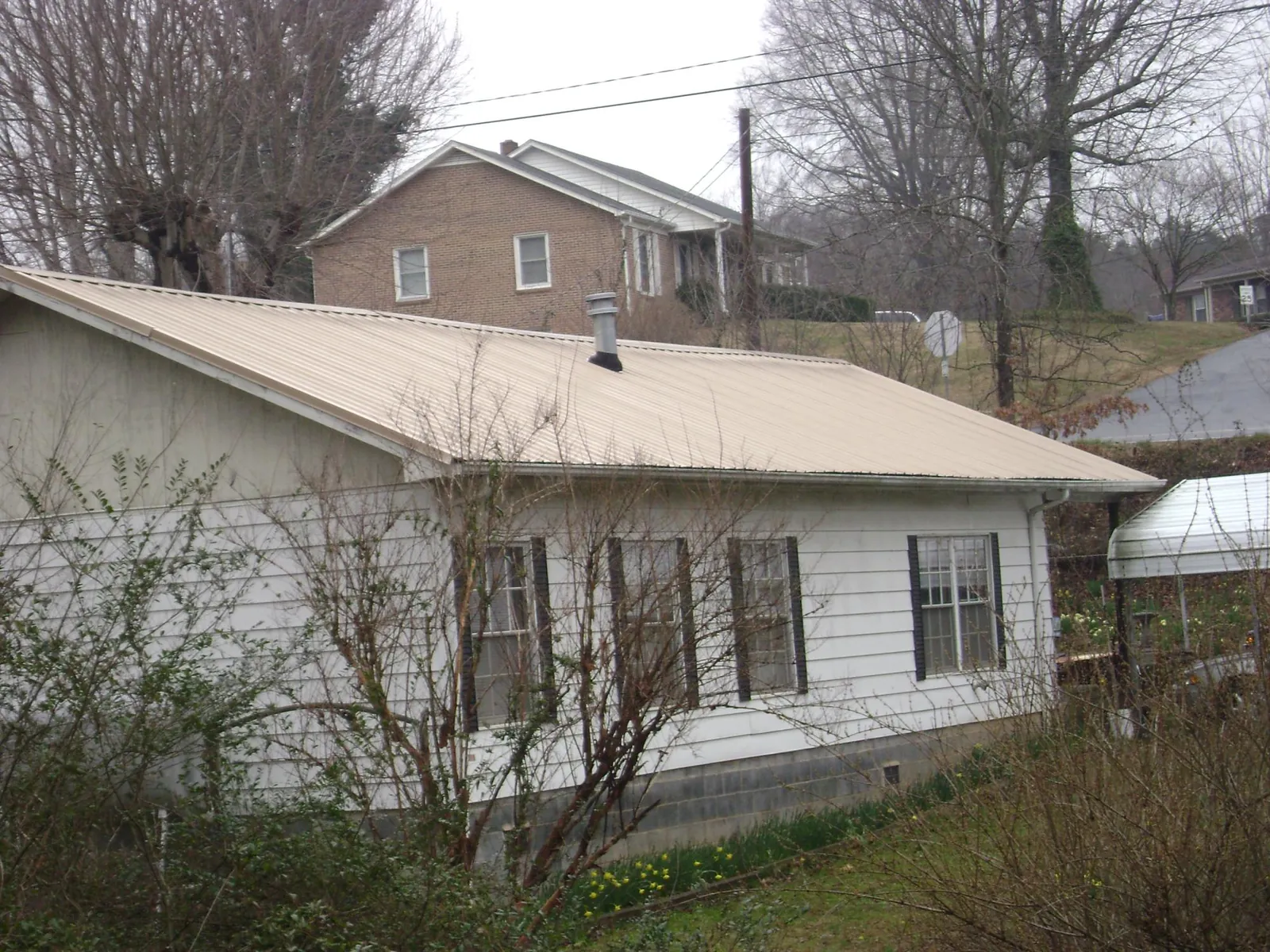 Tan metal roof on a white sided house set into a hillside — Commercial Roofing by Roofing Brothers in Houlton
