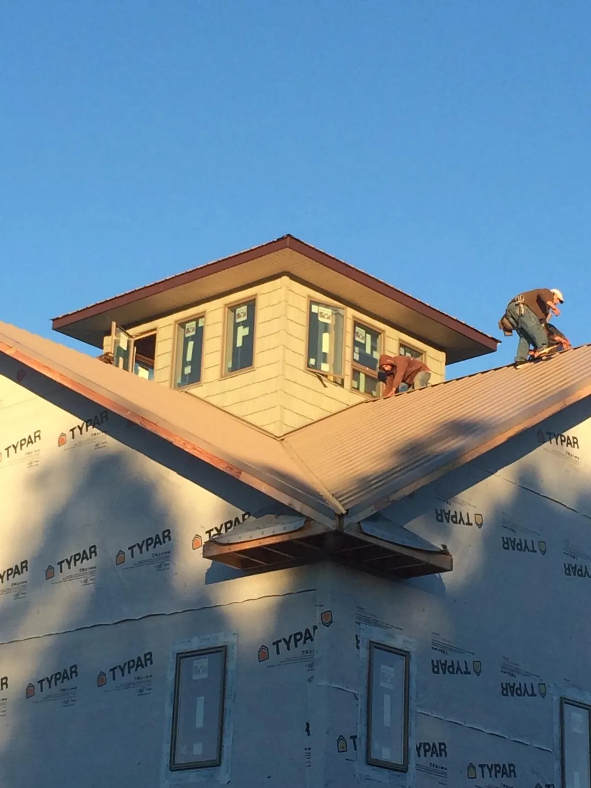 Roofers working around a rooftop cupola on a new metal roof at sunset — Roof Waterproofing in Houlton by Roofing Brothers